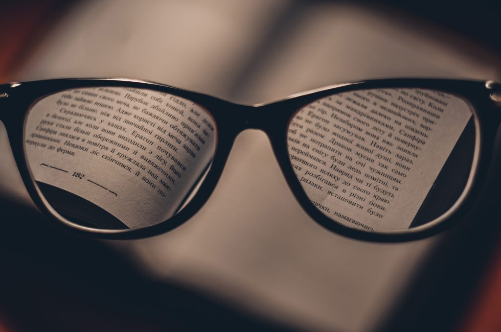 A pair of black rimmed glasses held in front of a book, bringing the words into focus.