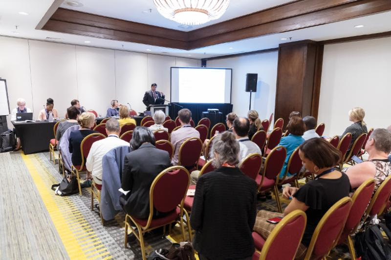 A room of people sitting and listening to a presentation.