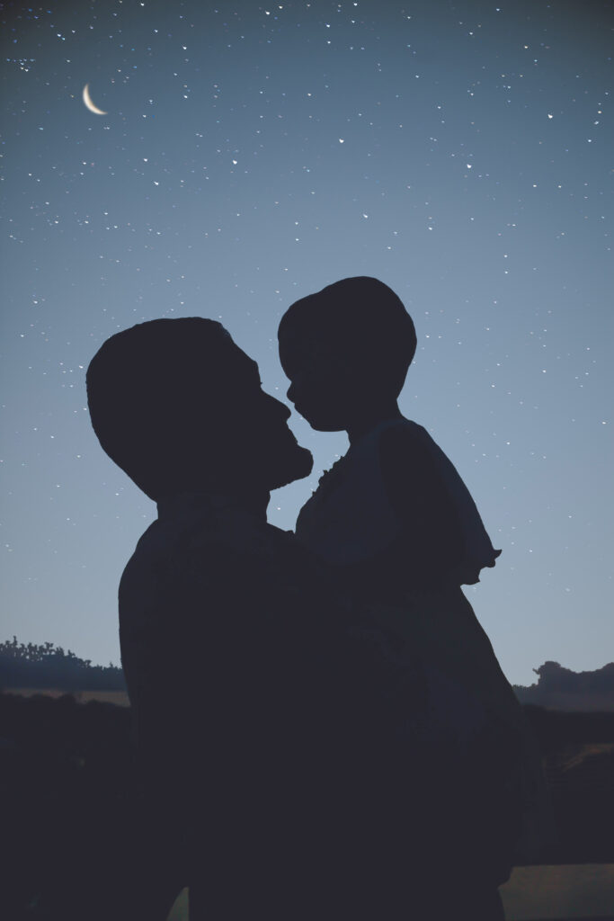 A man holds a child up to see the night sky.