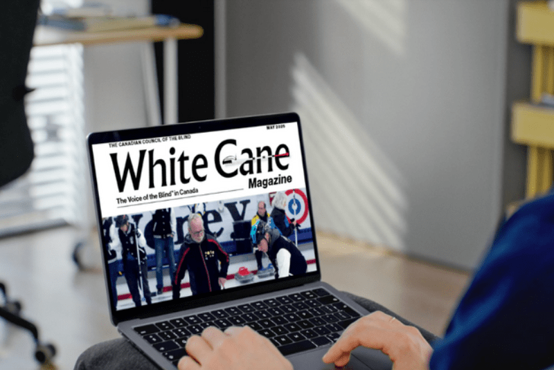 Close-up of a person using a laptop showing the White Cane Magazine cover featuring the Canadian Vision Impaired Curling Championship.