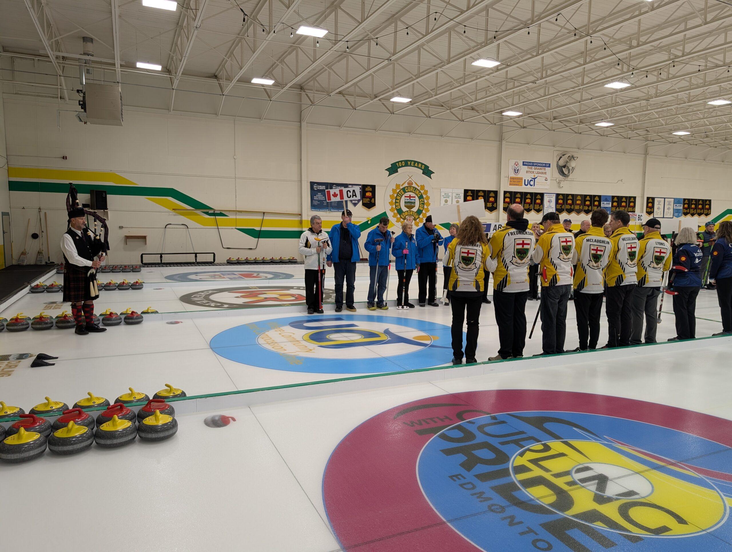 A photo of the 2026 CVICC opening ceremony: Curlers at the Granite Curling Club are lined up across from each other on the ice to the right of the photo. To the left is a person playing a bagpipe.