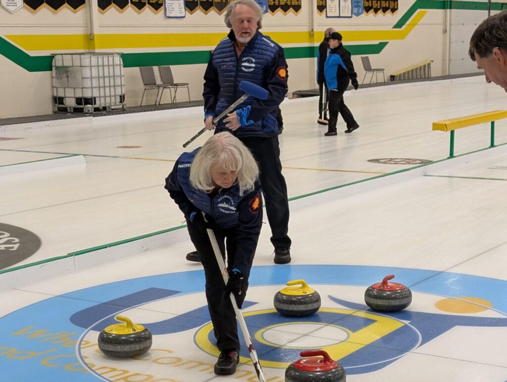Team Ontario players can be seen on the ice holding curling brooms and sweeping. Two yellow and two red stones are around them.