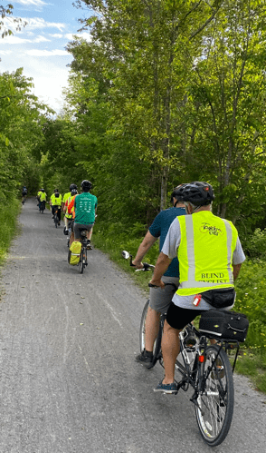 Several tandem bikes riding along a quiet tree-lined gravel road.