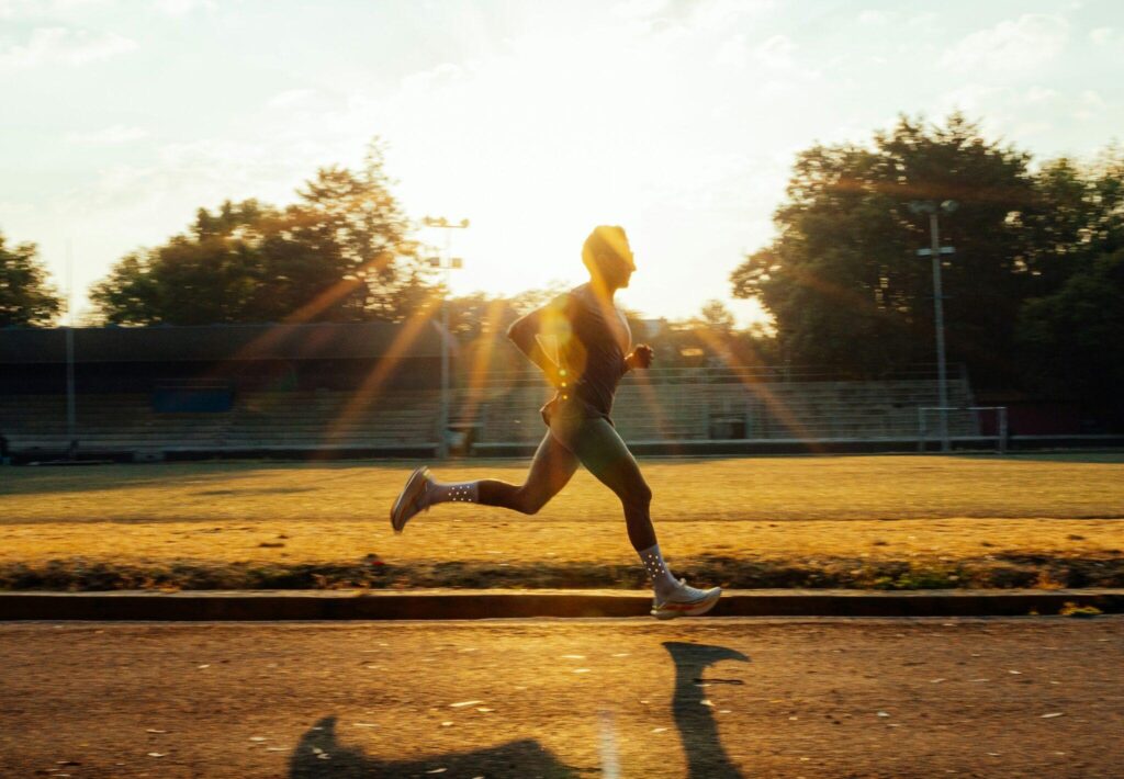 A person can be seen running on a field at dawn. The sun shines bright in the background.