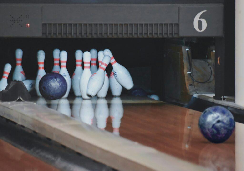 Close-up of a navy blue bowling ball striking a set of pins, with another bowling ball visible on the right.