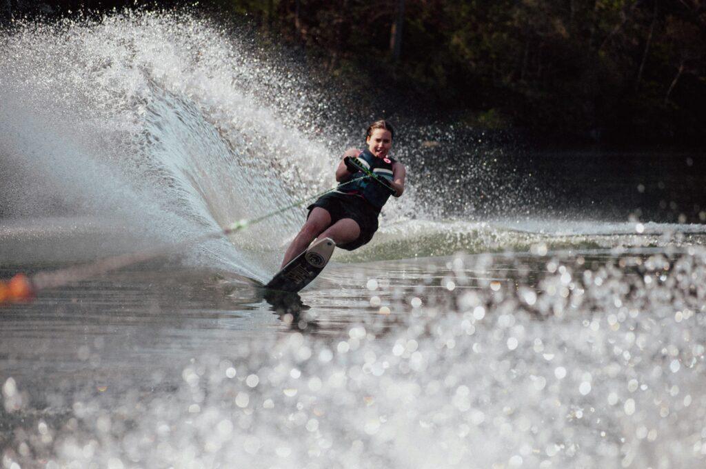 A person wearing a life jacket and shorts water skis across the water, holding a tow rope as water splashes around them on a sunny day.
